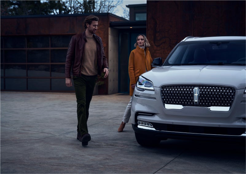 A man and a woman approaching a 2023 Lincoln Aviator® SUV, which illuminates certain lights when they are close | Karl Malone Lincoln in El Dorado AR