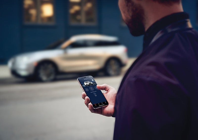 A person is shown interacting with a smartphone to connect to a Lincoln vehicle across the street. | Karl Malone Lincoln in El Dorado AR